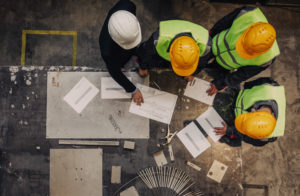 Workers and manager in safety helmets working with documents at factory